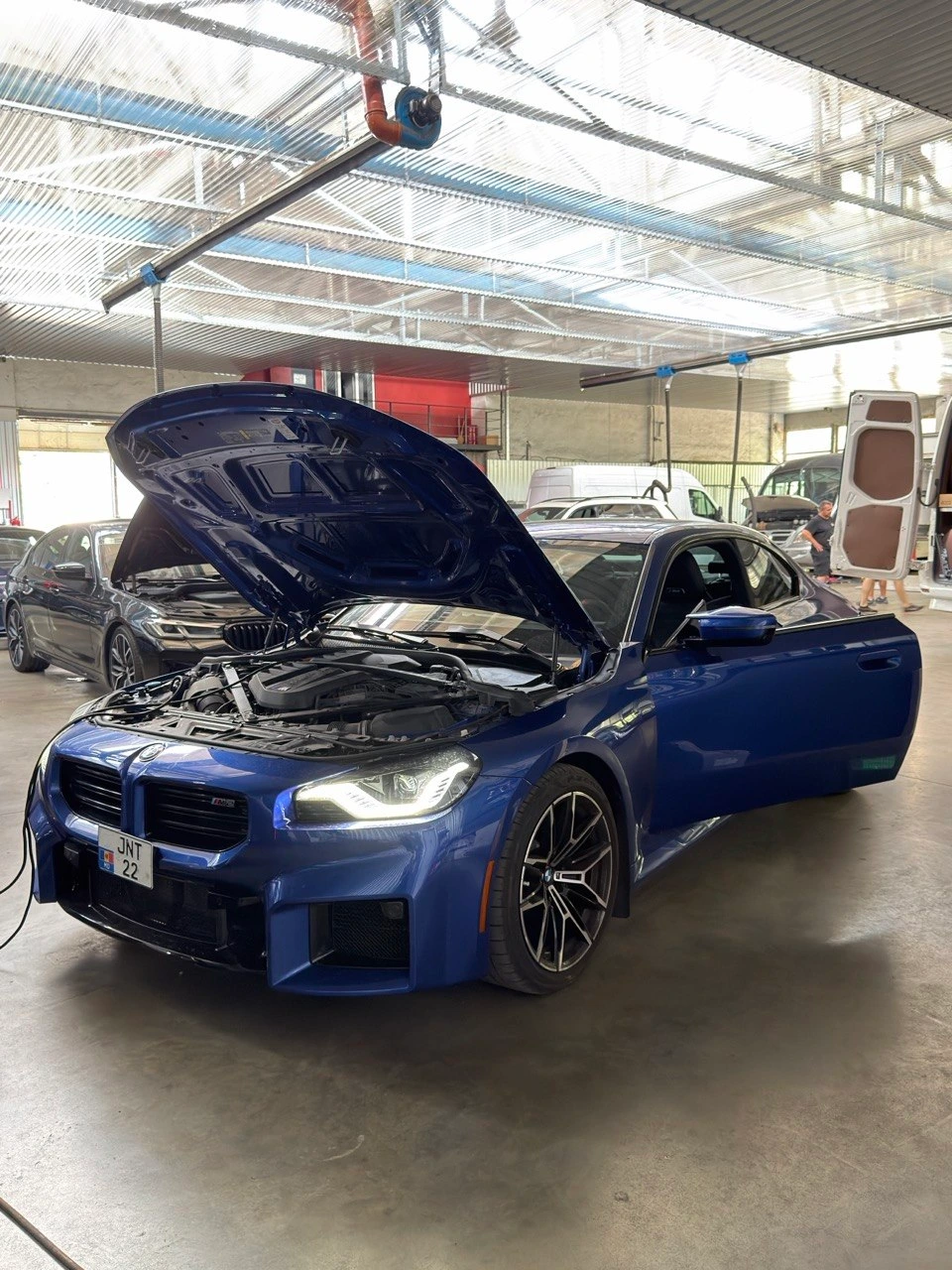 BMW M2 albastră cu capota deschisă în atelier