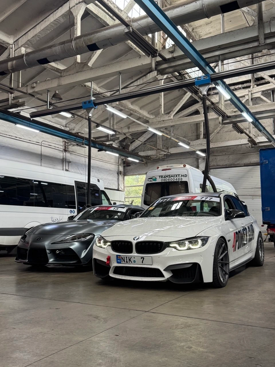 BMW M3 F80 albă a lui Nikita, cu numărul NIK 7, lângă o Toyota Supra în atelier